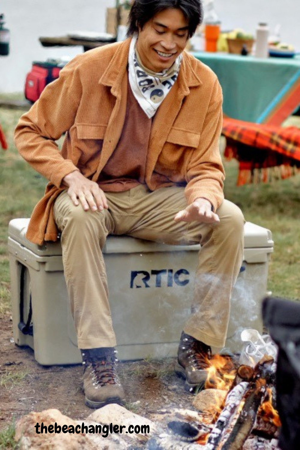 Man sitting on his RTIC 65 Hard Cooler by the campfire