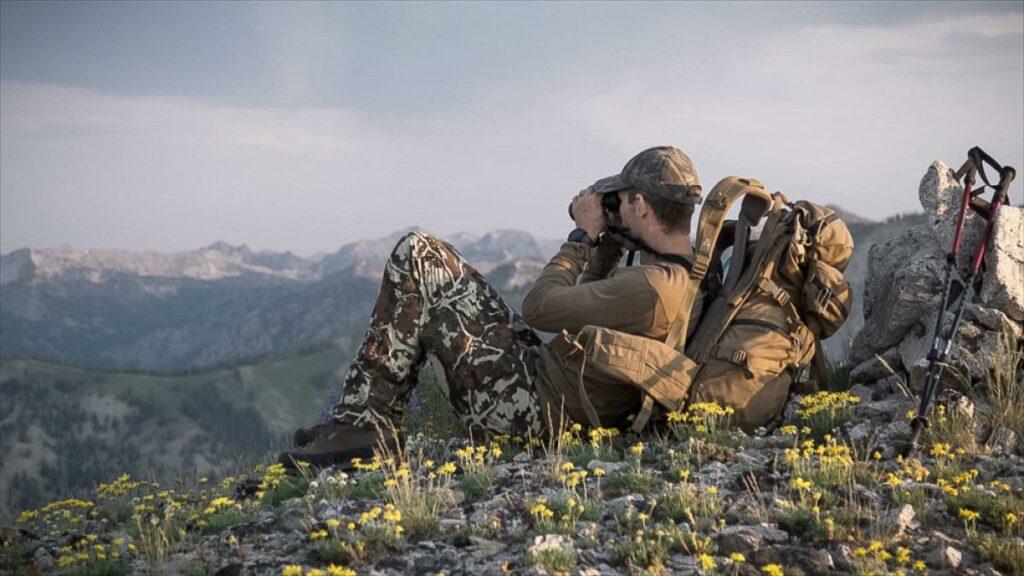 Man sitting on a high ridgeline doing some glassing and pre season scouting for the upcoming hunting seasons. REXING USA trail cameras