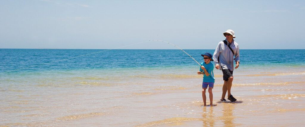 9 Essential Tips for surf fishing with kids - a dad watching his son fight a fish in the surf.