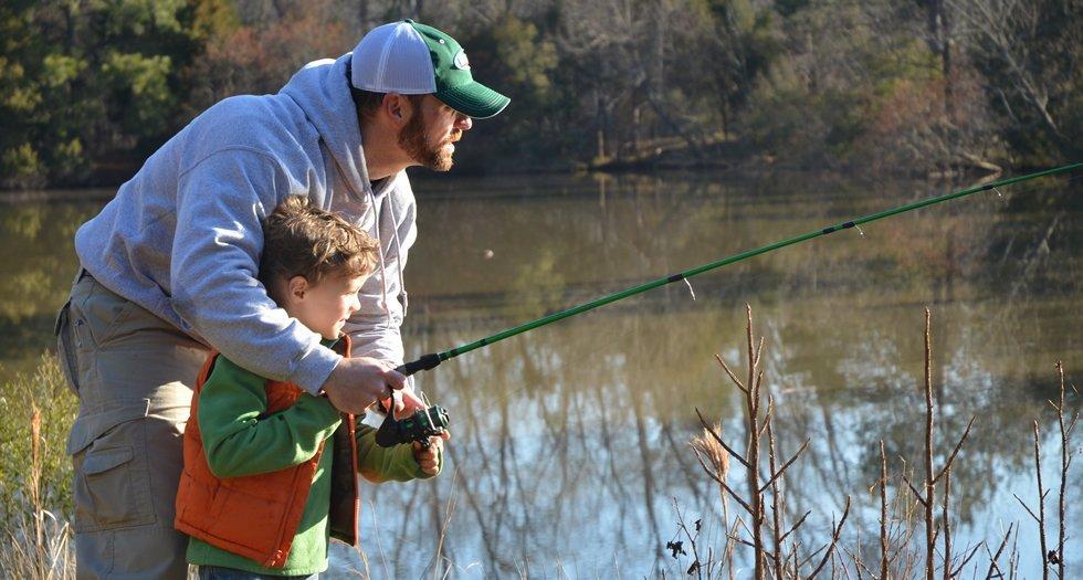 9 essential Tips for Surf Fishing with Kids - a dad teaching his son how to reel in a fish.