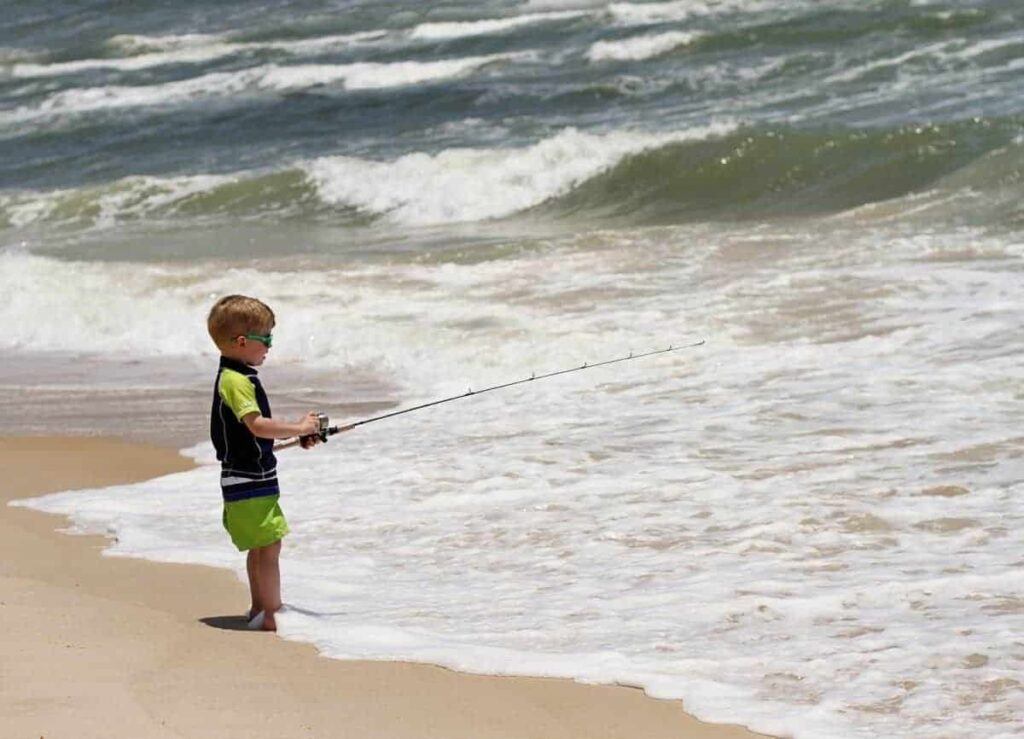 9 Essential Tips for Surf Fishing with kids - young boy with his open faced spinning combo fishing in the surf