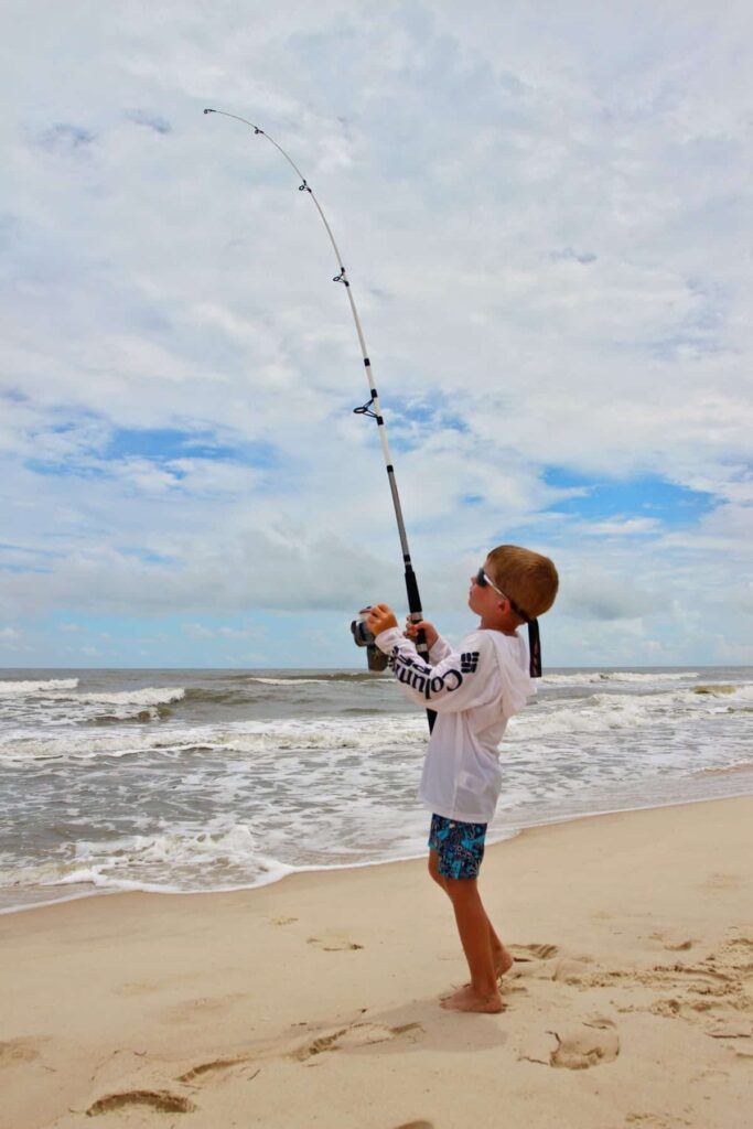 9 Essential Tips for Surf Fishing with Kids - Young boy hooked up with a nice fish in the surf