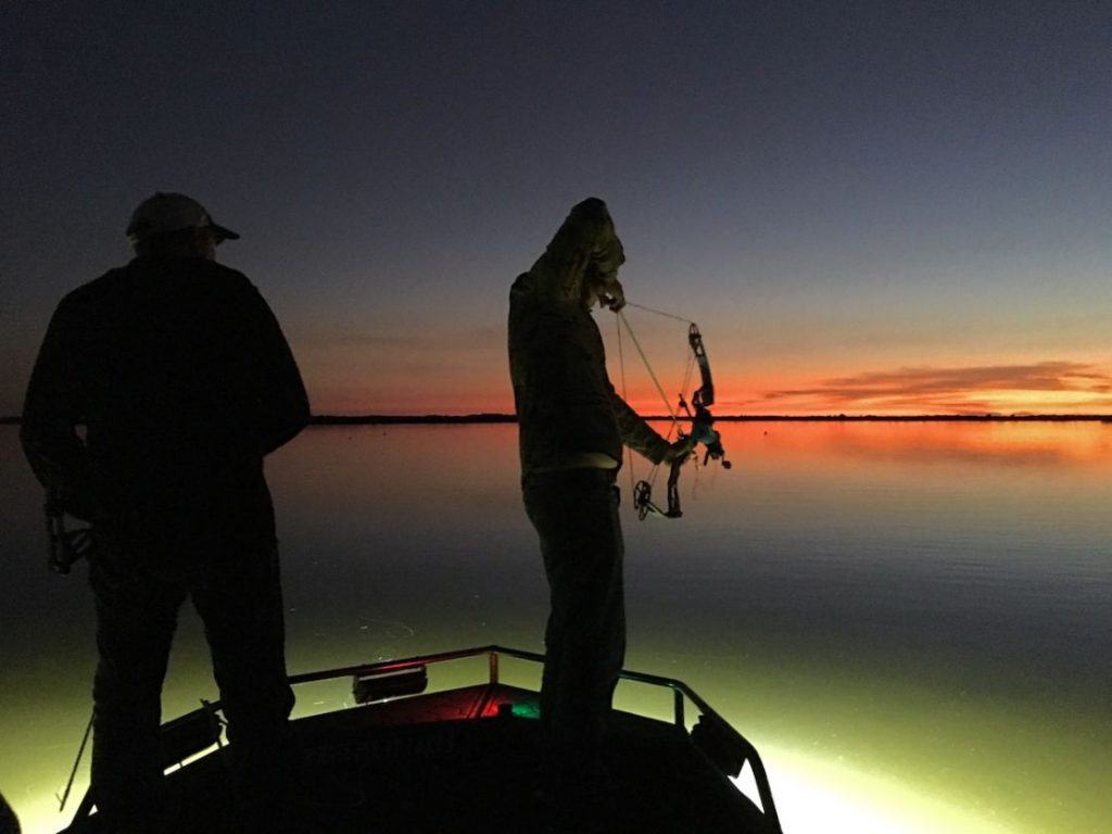 bowfishing how to for beginners - two bowfishermen taking aim from a boat at night