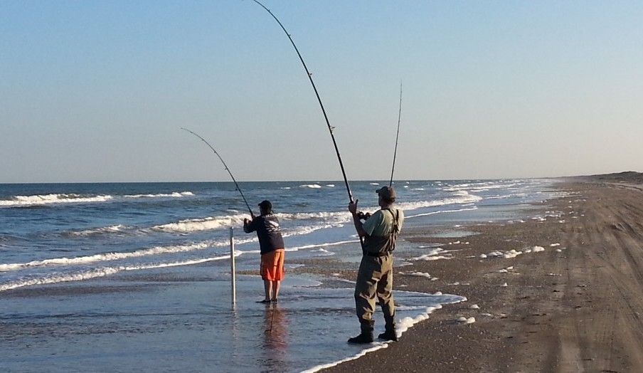 two fisherman hooked up and fighting fish on the beach