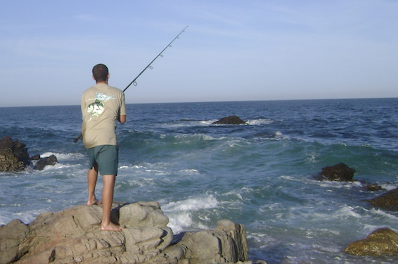 surf fishing in mexico - fisherman casting from a rocky shore into the surf