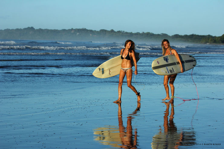 Two lady surfers walking down the beach carrying their surf boards in Costa Rica