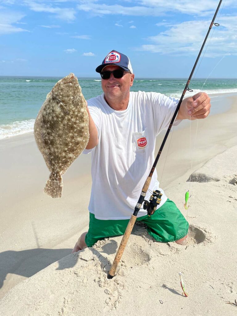 Angler kneeling in the sand at the beach with a nice flounder caught surf fishing