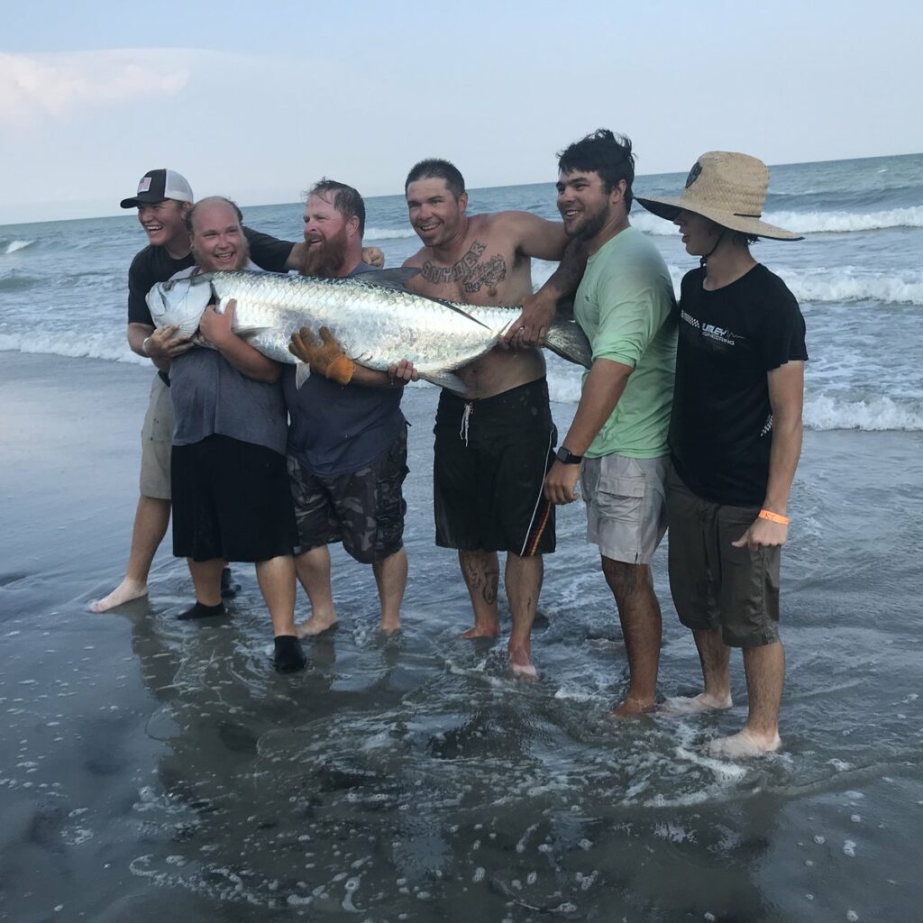 anglers holding a large tarpon caught while surf fishing in Myrtle Beach South Carolina