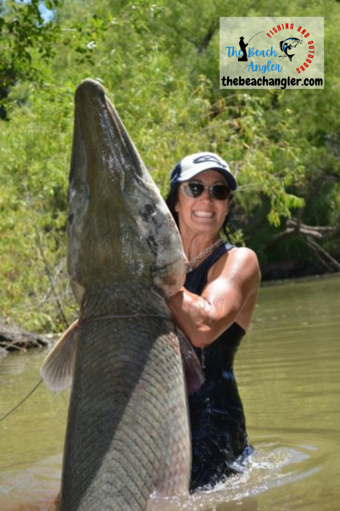 Fishing for Alligator Gar - Lady angler standing waist deep in the river holding up a huge alligator gar