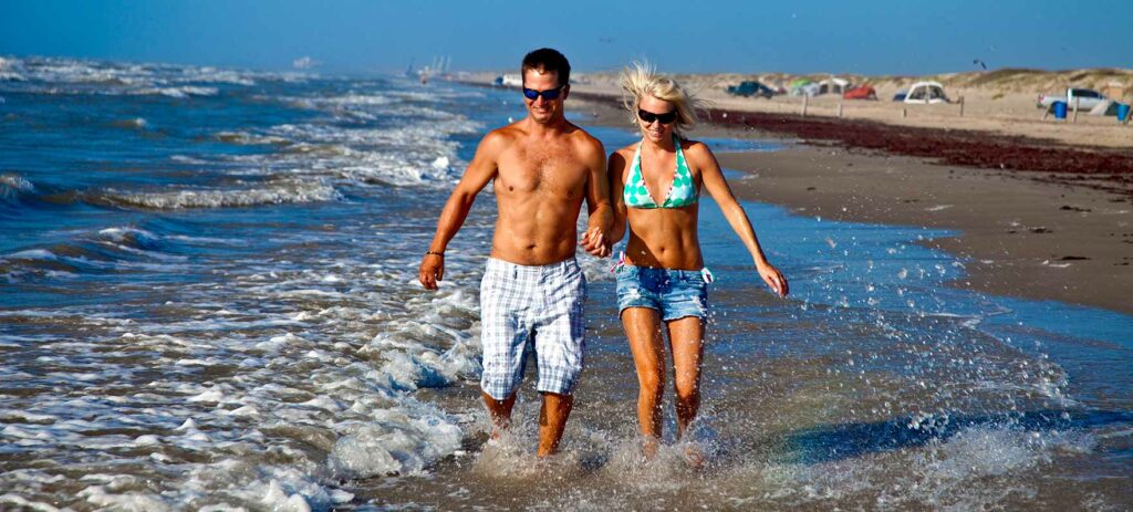 Couple holding hands and wading in the surf at Mustang Island State Park in Texas