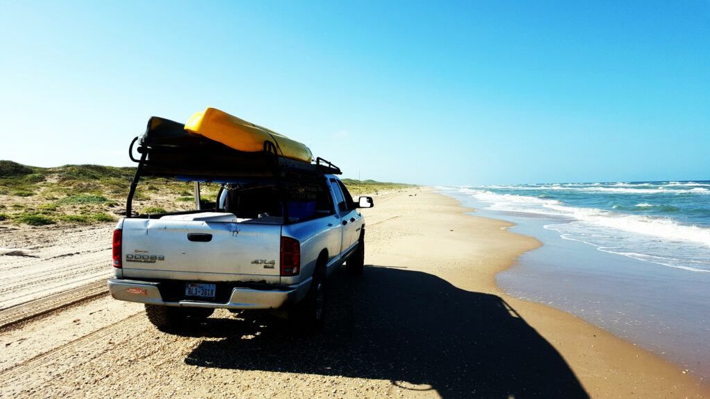 Kayaks loaded on the shark rack that is on a pickup at the beach