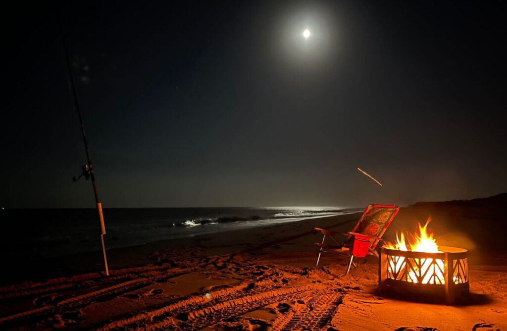 surf fishing at night on the beach with a campfire and the moon and surf in the background