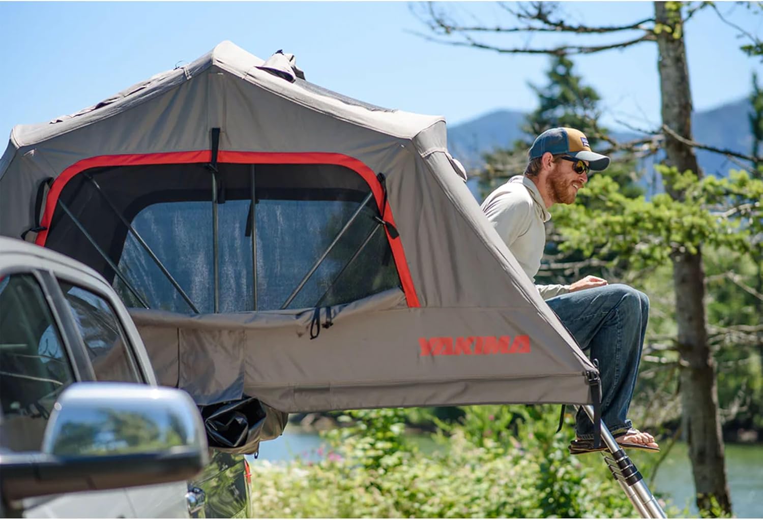 Yakima Skyrise Medium Rooftop Tent mounted on a pickup with a man sitting in the doorway at the top of the ladder.